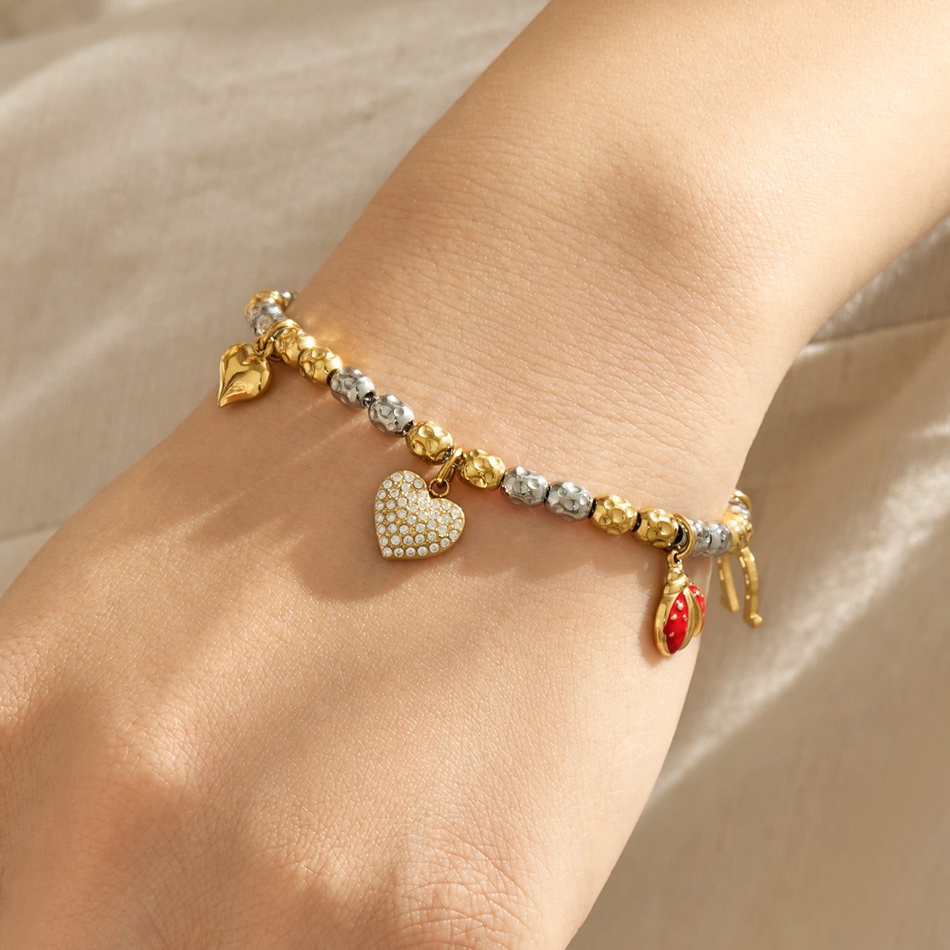 Gold charm bracelet with heart and colorful pendant details worn on the wrist