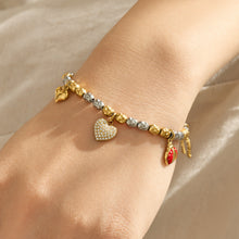 Gold charm bracelet with heart and colorful pendant details worn on the wrist