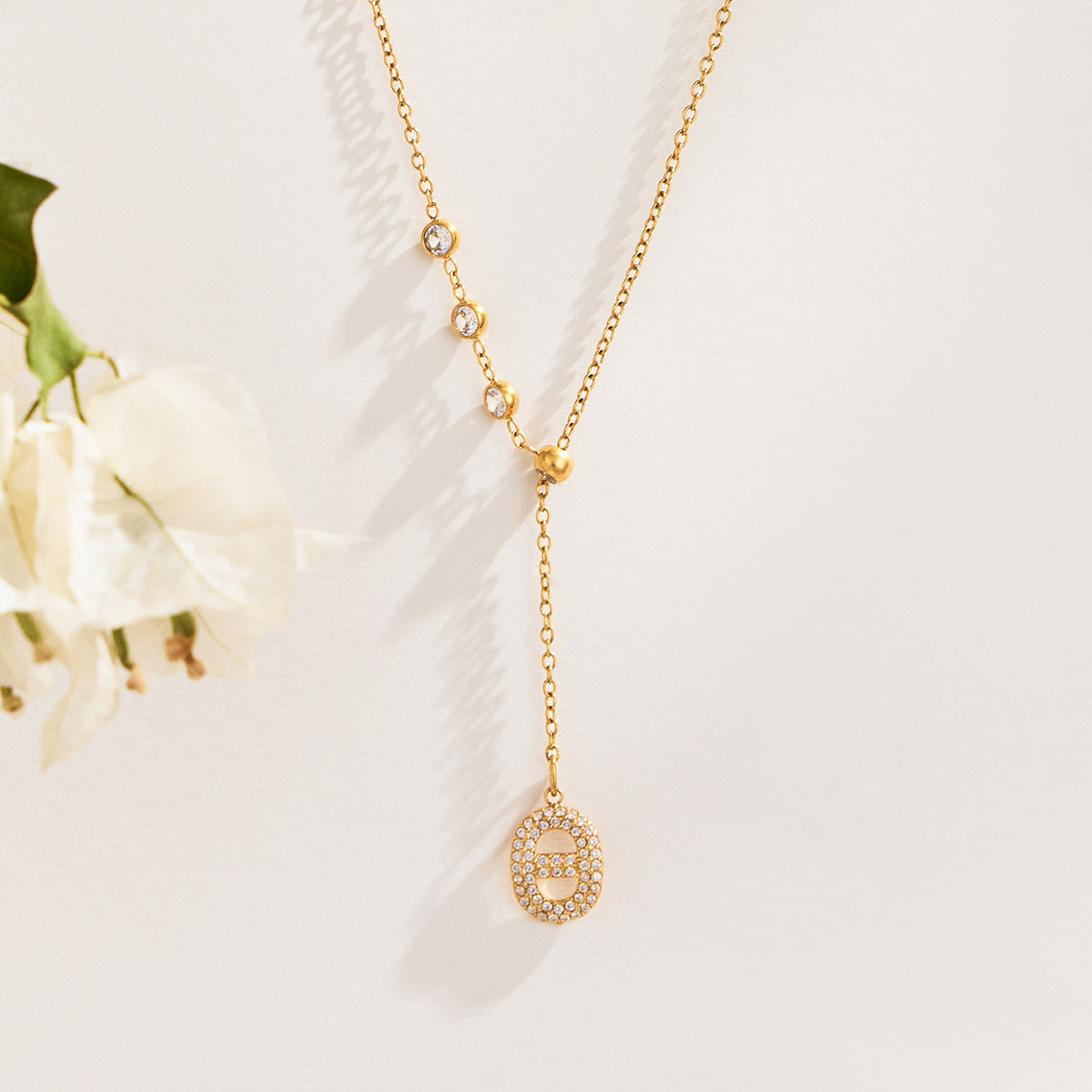 Gold-tone zircon Y drop necklace with round stone accents displayed with white flowers