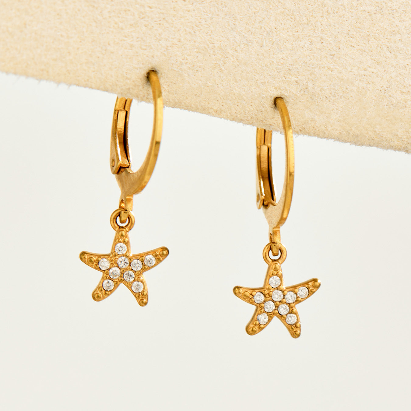 Pair of gold zirconia starfish charm huggie earrings displayed on a neutral background