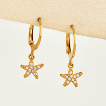 Pair of gold zirconia starfish charm huggie earrings displayed on a neutral background
